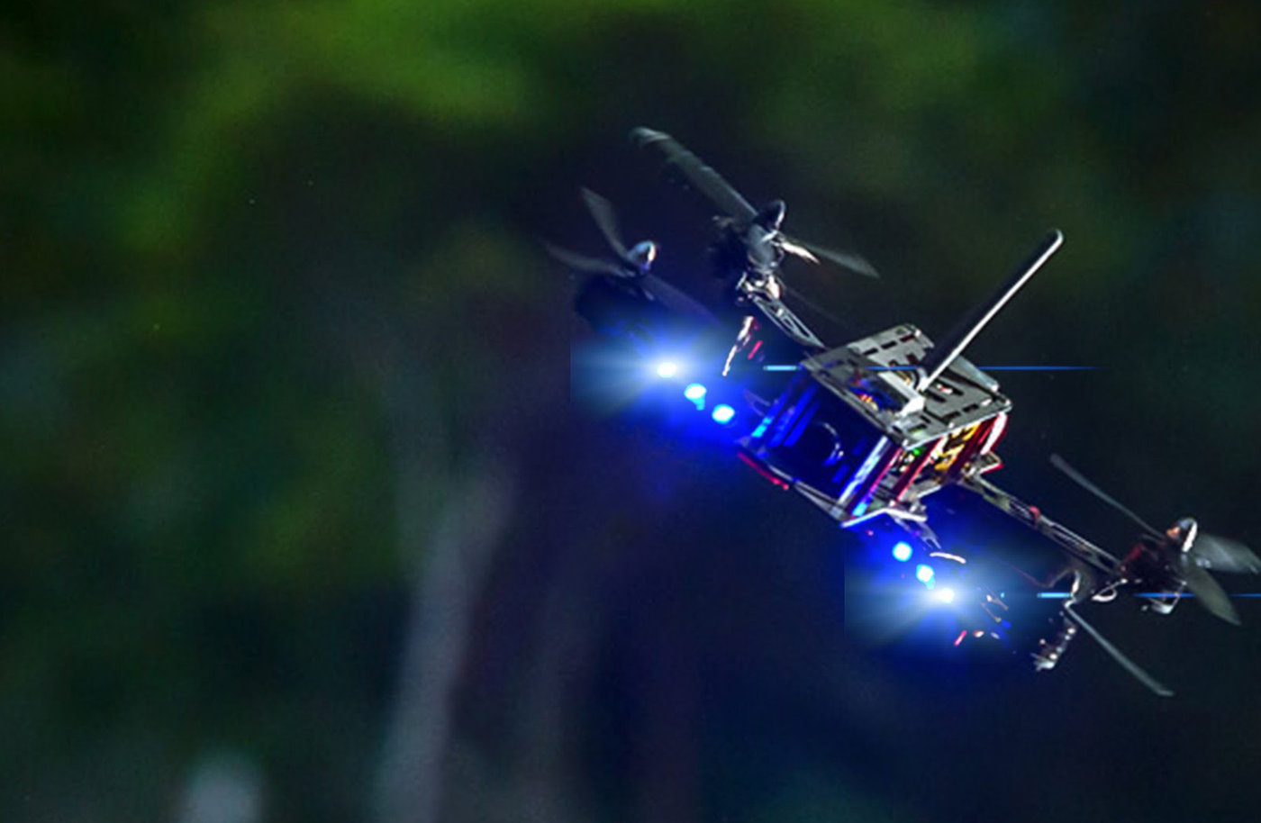 Racing quad with LEDs lit, banking through trees